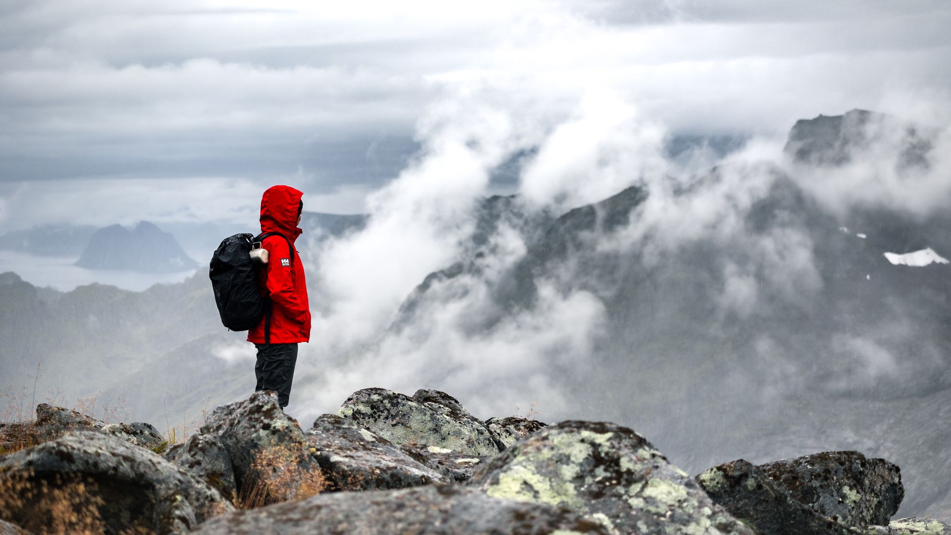 霧の山頂に立つ赤いジャケットの登山者
